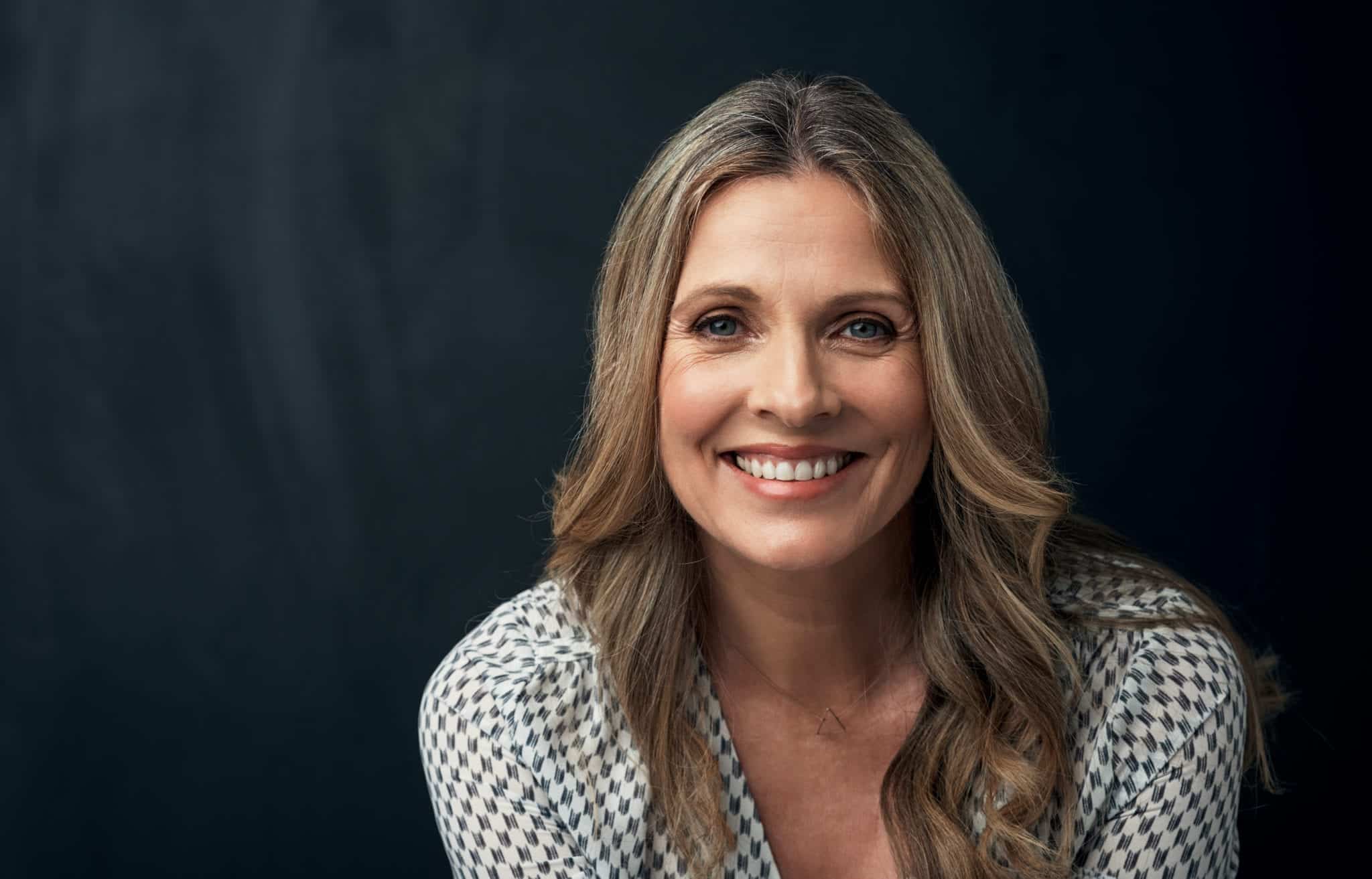 headfshot of smiling blonde woman with dark background