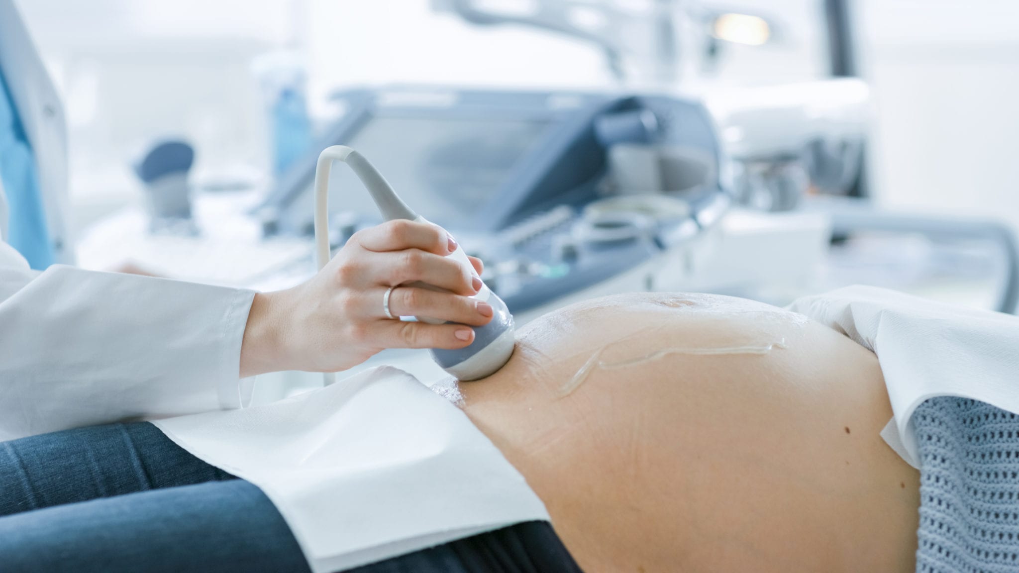 In the Hospital, Close-up Shot of the Doctor Doing Ultrasound / Sonogram Scan to a Pregnant Woman. Obstetrician Moving Transducer on the Belly of the Future Mother.