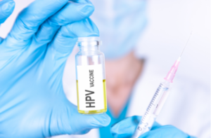 HPV VACCINE of is written on a bottle with the background of a doctor with a syringe