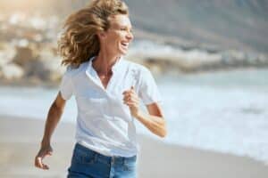 Cheerful,Mature,Woman,Running,On,The,Beach,On,A,Sunny