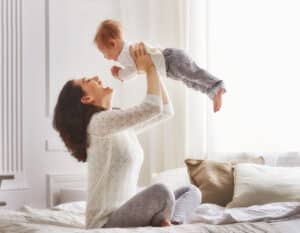 A postpartum woman holding her baby in the air and laughing